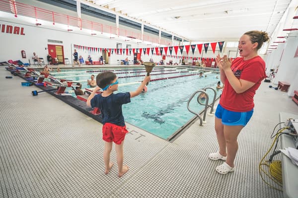 Student ringing the advancement bell as coach celebrates behind them at Old City Swim School